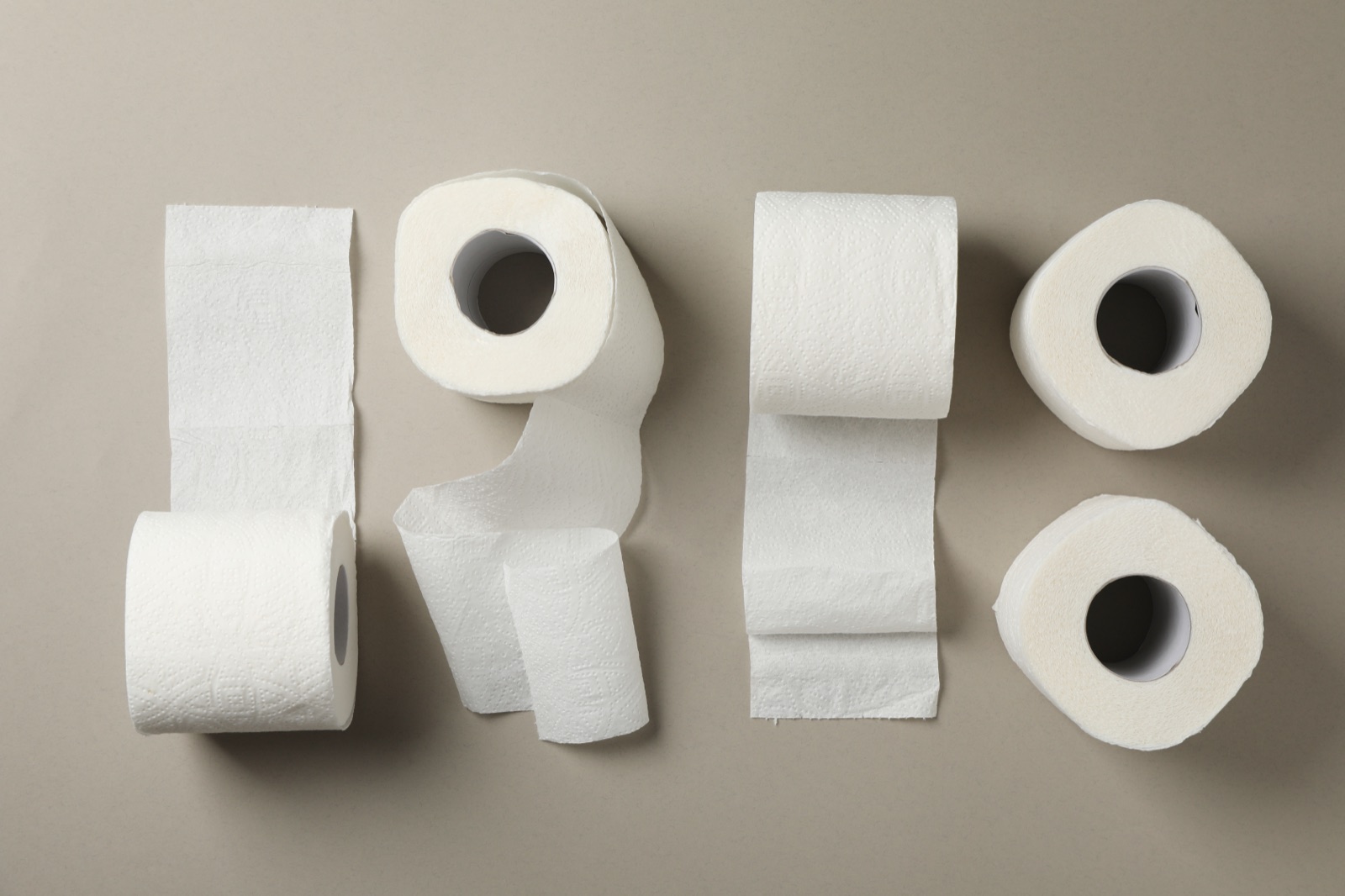Varios rollos de papel higiénico blanco, algunos desenrollados, sobre una mesa gris en vista cenital